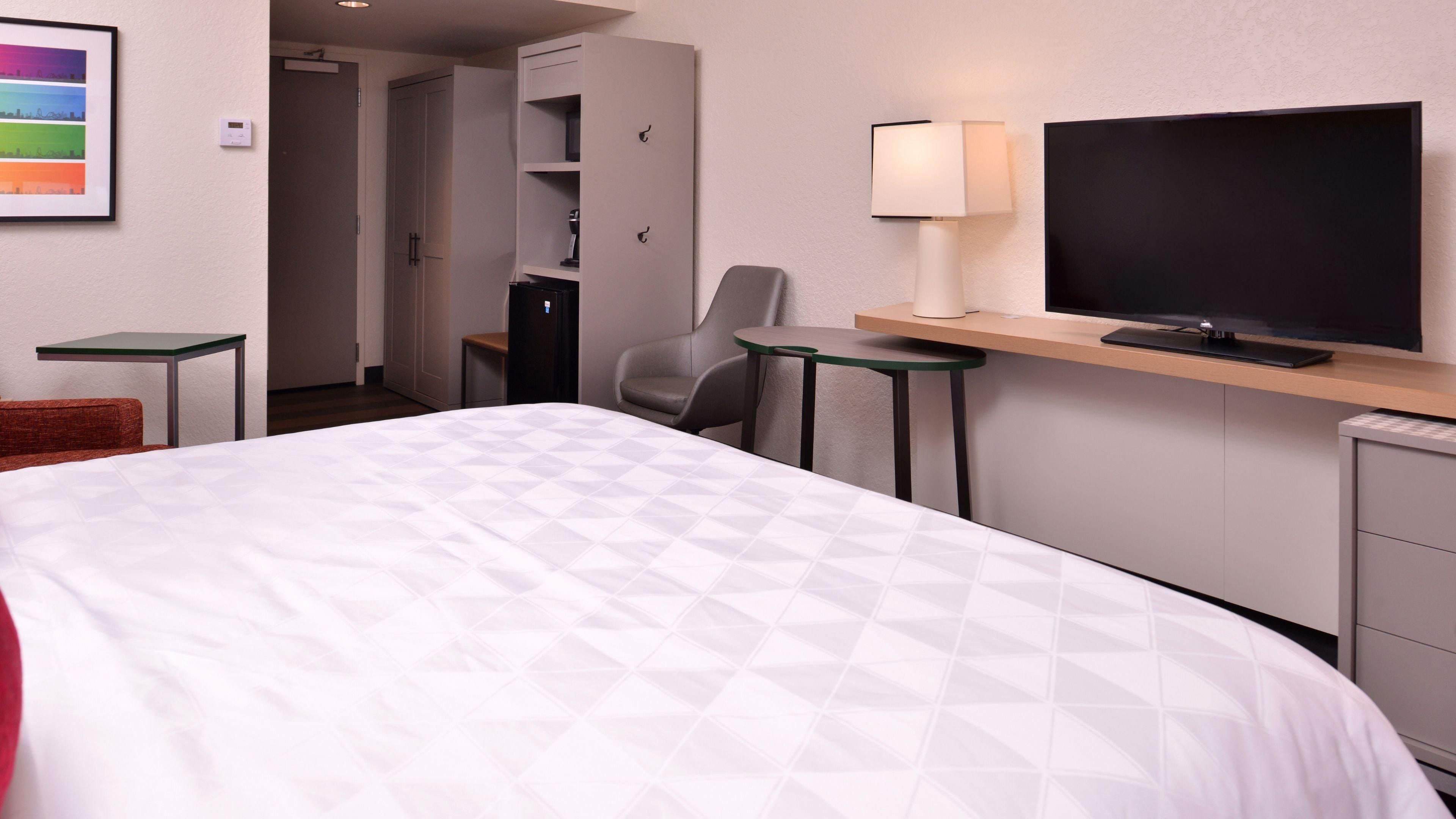 A hotel room with a bed, a desk with a TV, a chair, a small table, and a wardrobe.