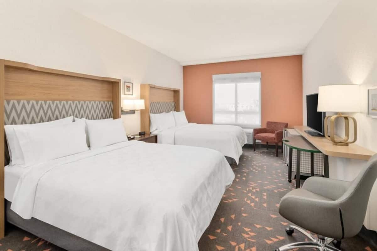 Ein Hotelzimmer mit zwei Betten, einem Schreibtisch, einem Sessel, einem Fernseher und einem Fenster.