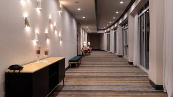 A hotel corridor with a reception desk, seating area, and large windows.