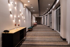 A hotel corridor with a reception desk, seating area, and large windows.