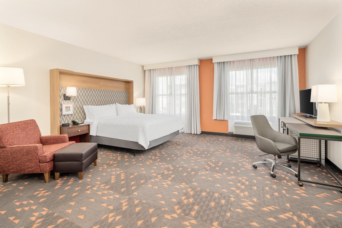 A hotel room with a bed, a desk, a chair, a sofa, and a carpet with a geometric pattern.