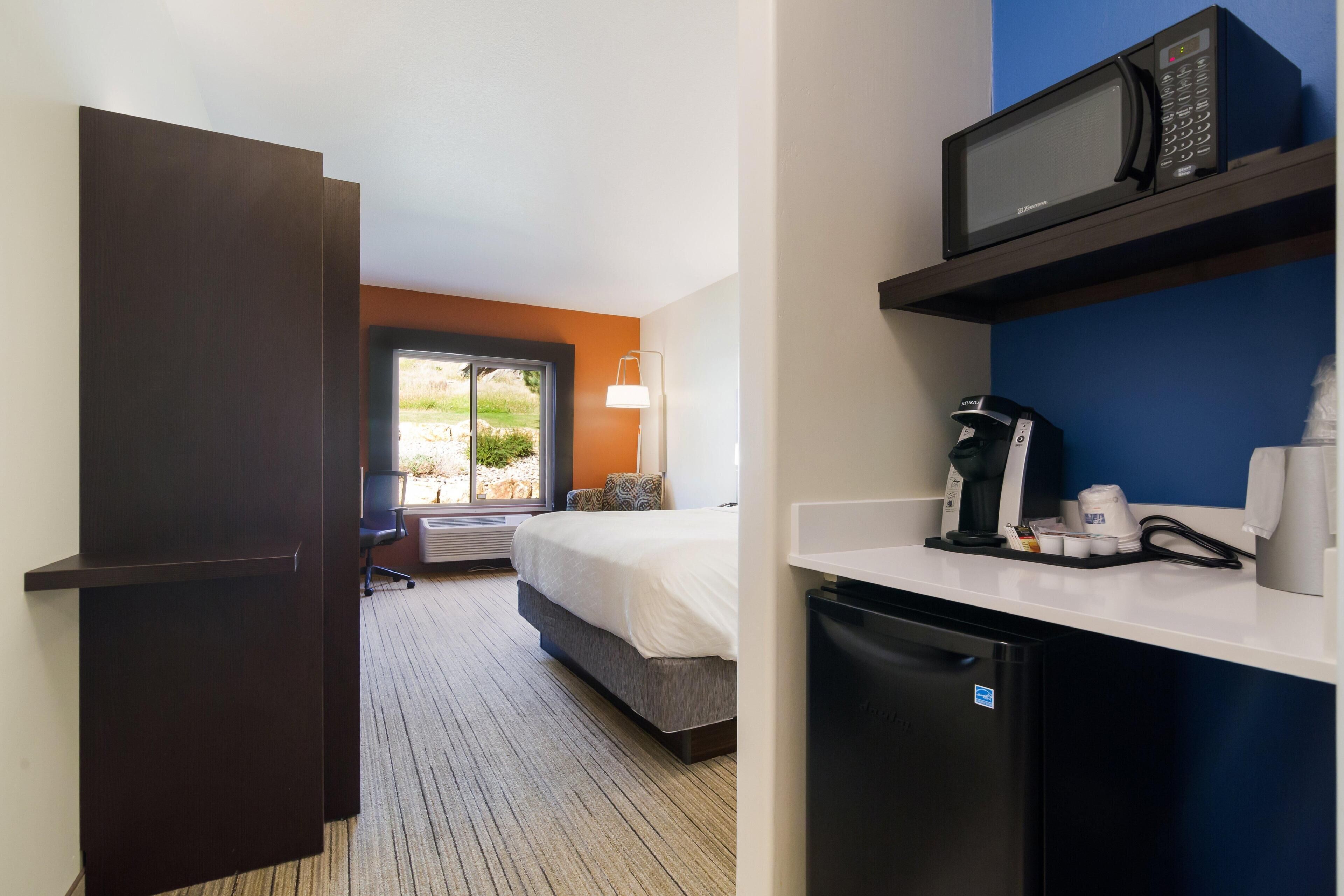 Een hotelkamer met een bed, een klein kitchenette met een magnetron, een koffiezetapparaat en een koelkast. Er is een raam met uitzicht op groen.