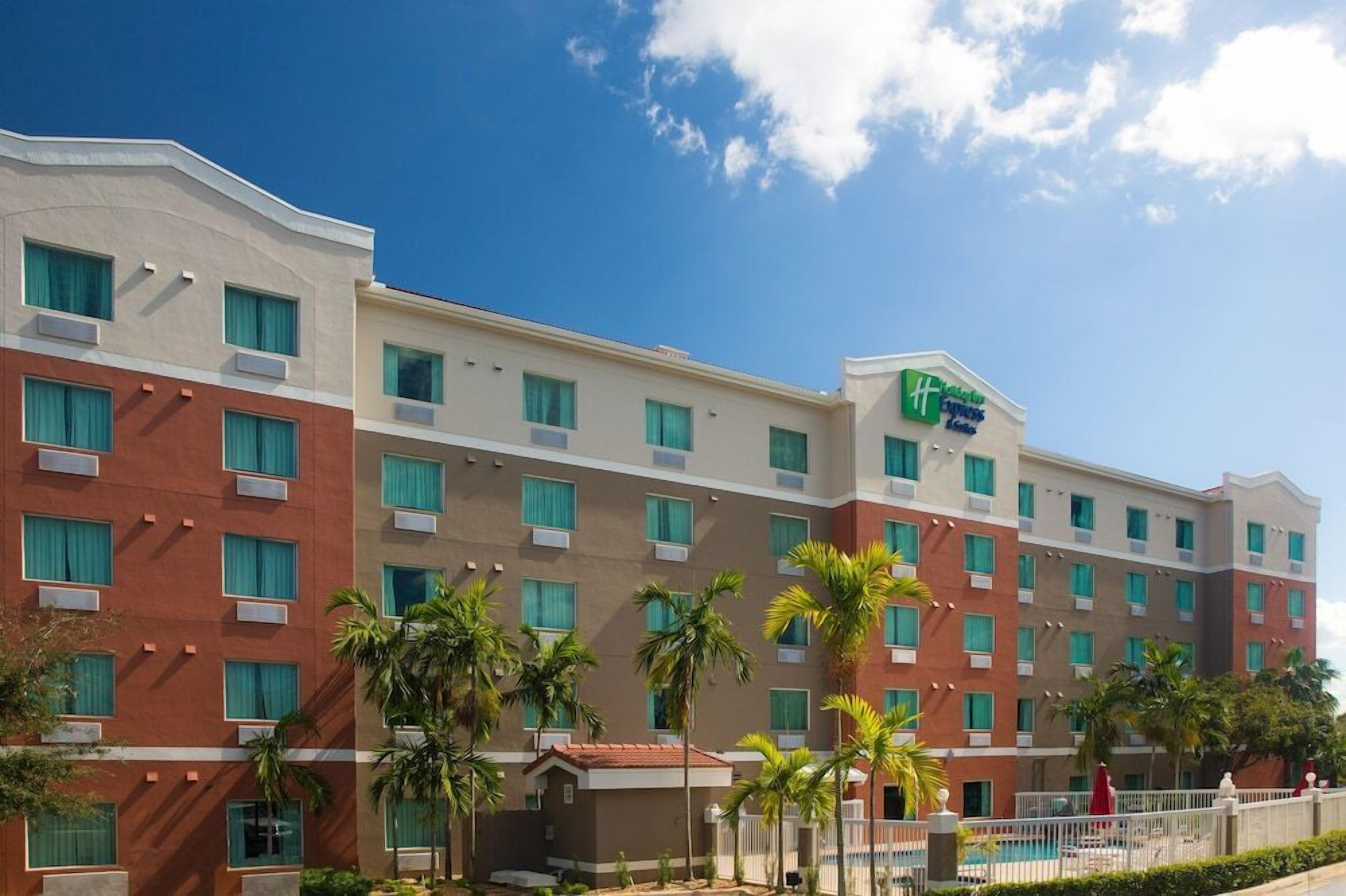 Un hotel de varios pisos con un diseño moderno, que presenta un llamativo logo verde y azul en la fachada.