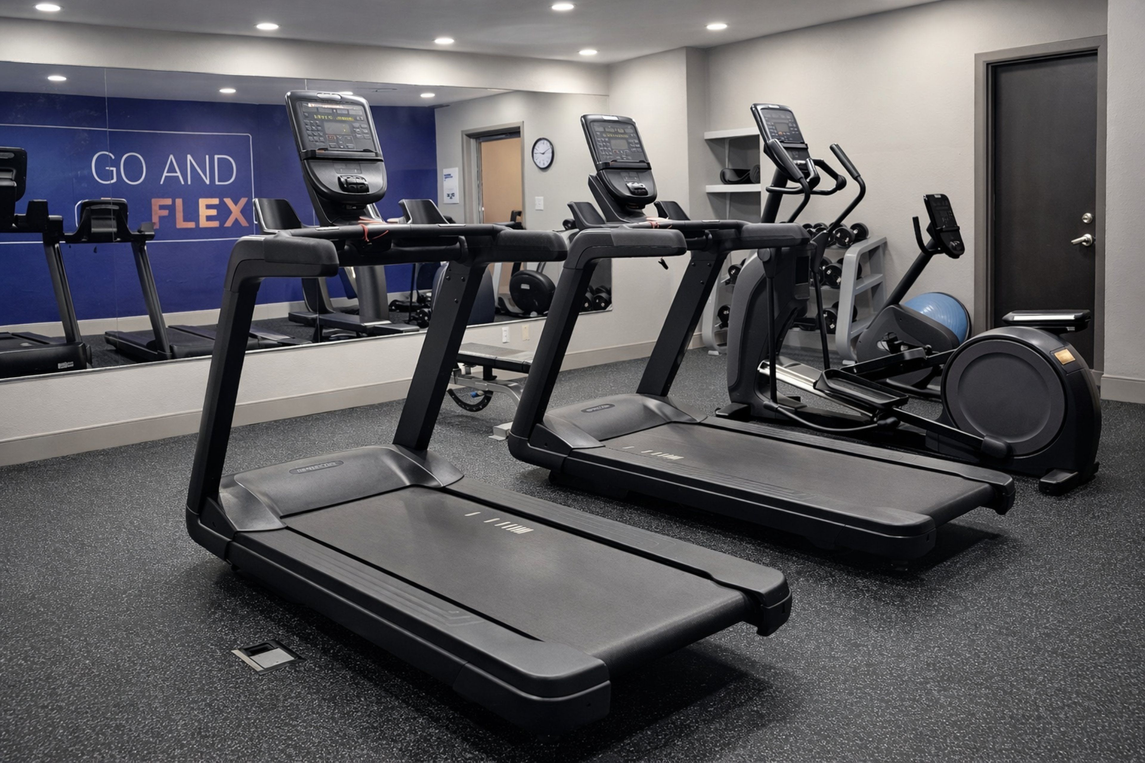 A gym with treadmills, a wall with motivational text, and a door.