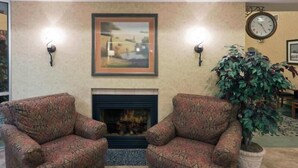 A living room with two patterned armchairs, a fireplace, a framed painting, a clock, and a potted plant. - Holiday Inn Express & Suites Pierre-fort Pierre (Fort Pierre)