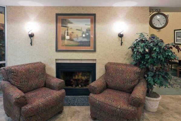 A living room with two patterned armchairs, a fireplace, a framed painting, a clock, and a potted plant. - Holiday Inn Express & Suites Pierre-fort Pierre (Fort Pierre)