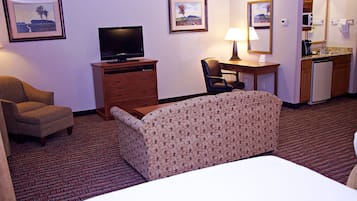 Quarto de hotel com cama, escrivaninha, cadeira, televisão e cozinha compacta.
