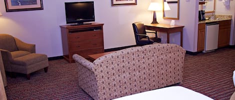 A hotel room with a bed, a desk, a chair, a television, and a kitchenette.