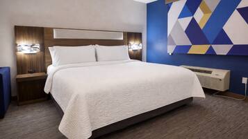 A hotel room with a large bed, wooden headboard, bedside lamps, and a wall-mounted air conditioner.