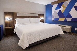 A hotel room with a large bed, wooden headboard, bedside lamps, and a wall-mounted air conditioner. - Holiday Inn Express & Suites Pierre-fort Pierre (Fort Pierre)