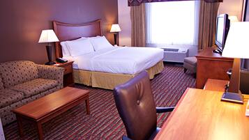 A hotel room with a bed, a sofa, a desk, a chair, a TV, and a lamp.