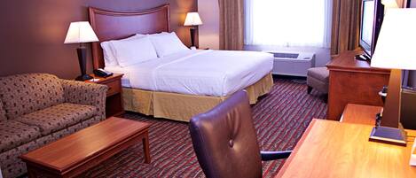 A hotel room with a bed, a sofa, a desk, a chair, a TV, and a lamp.