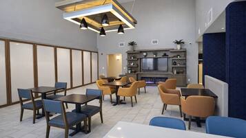 A modern interior with tables and chairs, a fireplace, and a kitchen area.