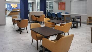 A modern dining area with tables and chairs, a reception desk, and a large window.