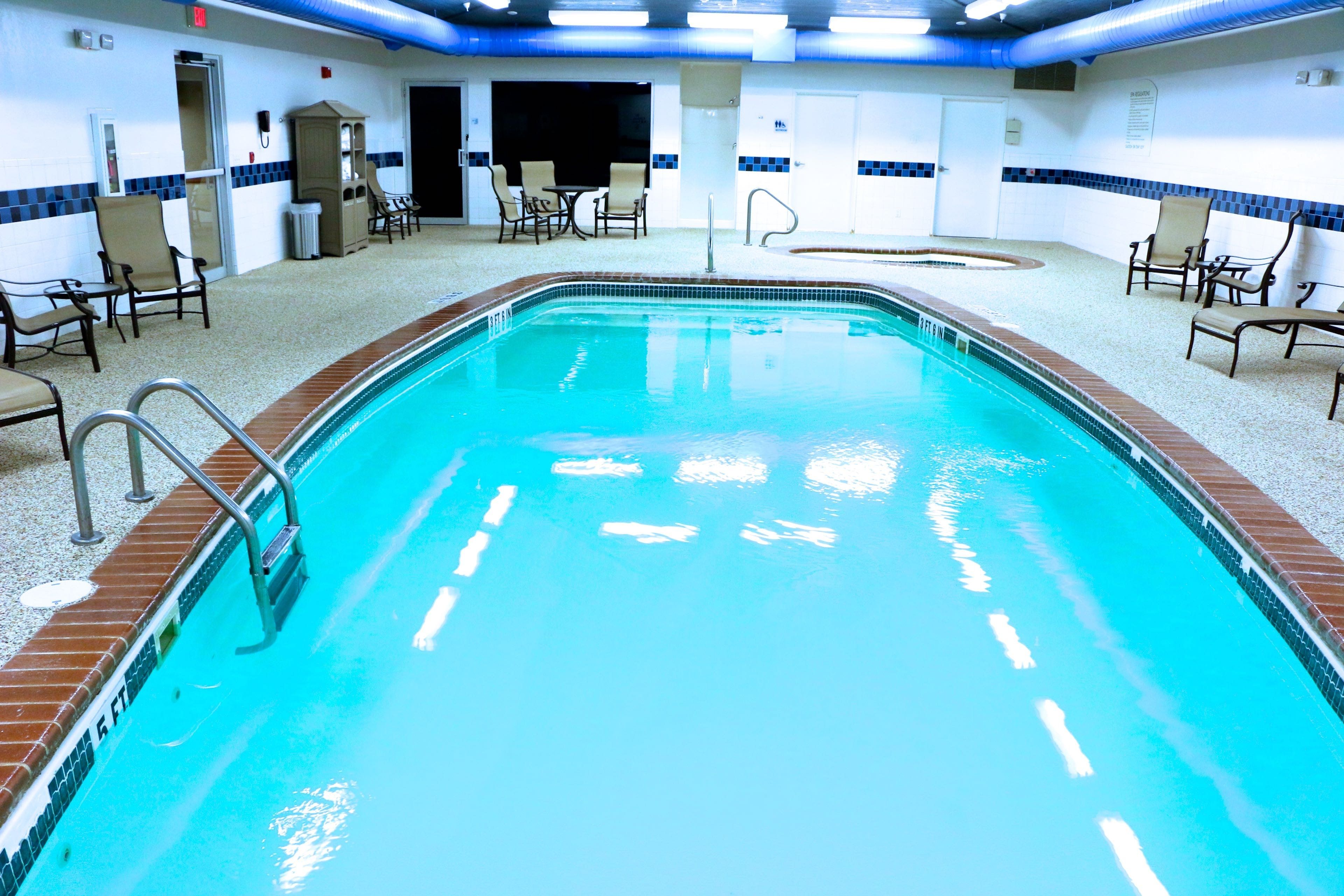 Una piscina interna con superficie d'acqua trasparente, circondata da sdraio e un pavimento piastrellato.