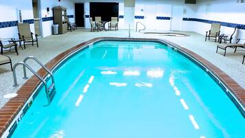 Una piscina interna con superficie d'acqua trasparente, circondata da sdraio e un pavimento piastrellato.