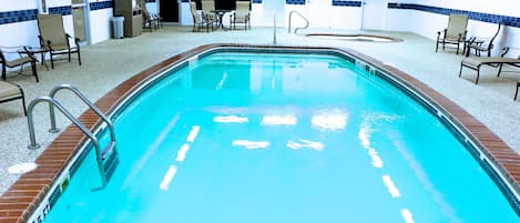 Una piscina interior con superficie de agua cristalina, rodeada de sillas de descanso y un suelo de baldosas.