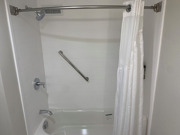 Un bagno con doccia, una barra di sostegno e una tenda.