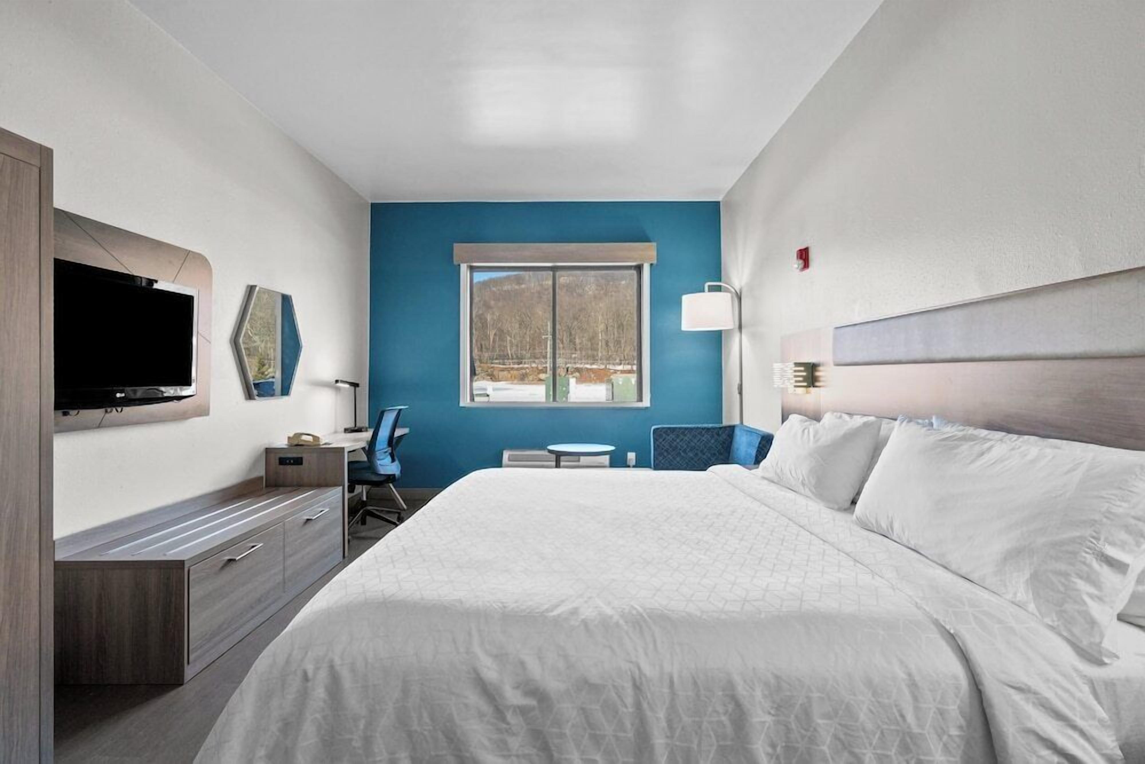 Habitación de hotel con una cama grande, televisor montado en la pared, escritorio con una silla y ventana con vistas al exterior.