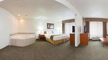 A hotel room with a large bed, a separate bathroom with a bathtub, a desk, a chair, and a TV.