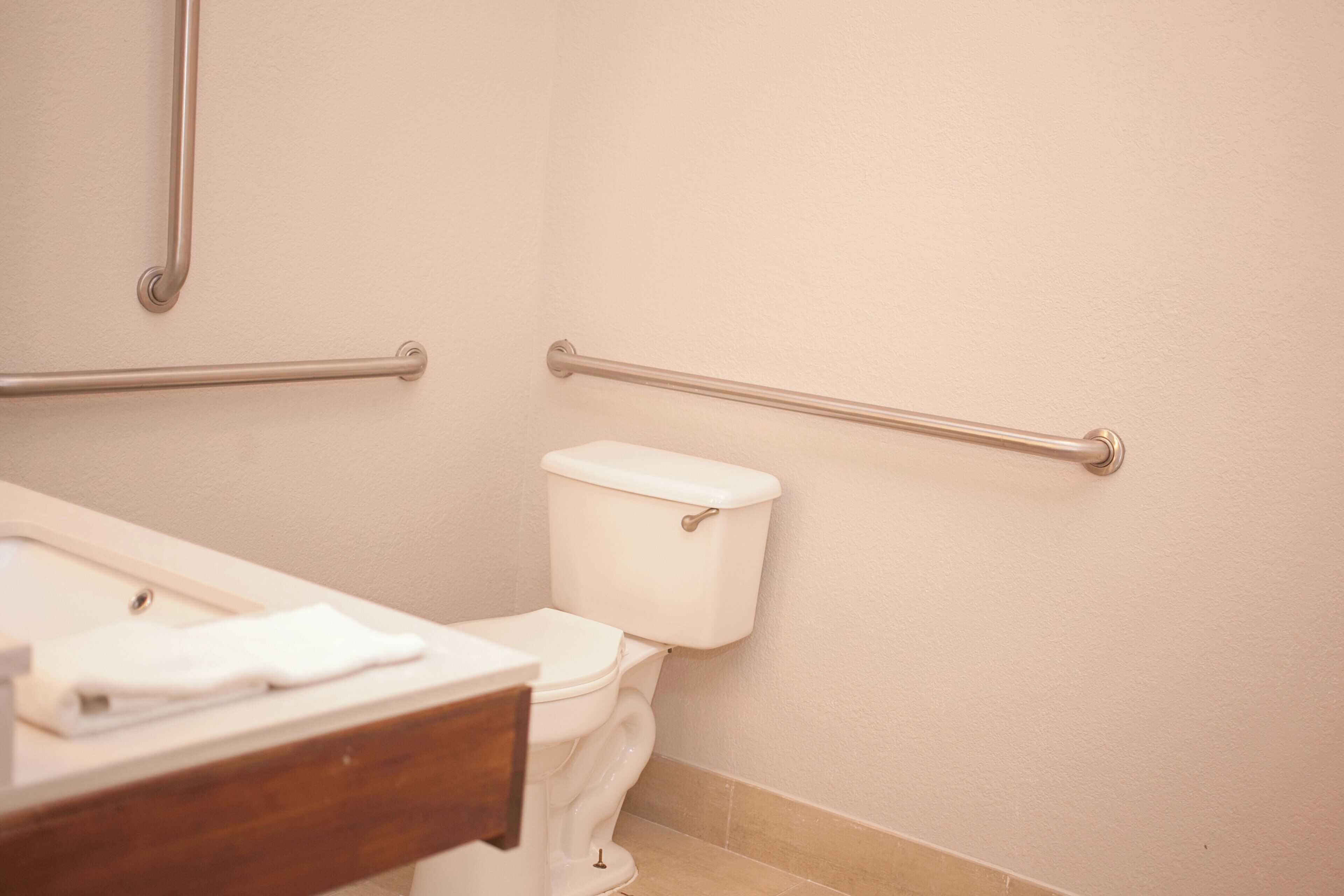 A bathroom with a toilet, grab bars, and a wooden vanity.