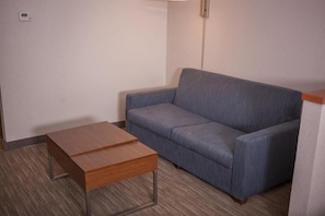 A small, modern room with a grey sofa, a wooden table, and a light switch on the wall.