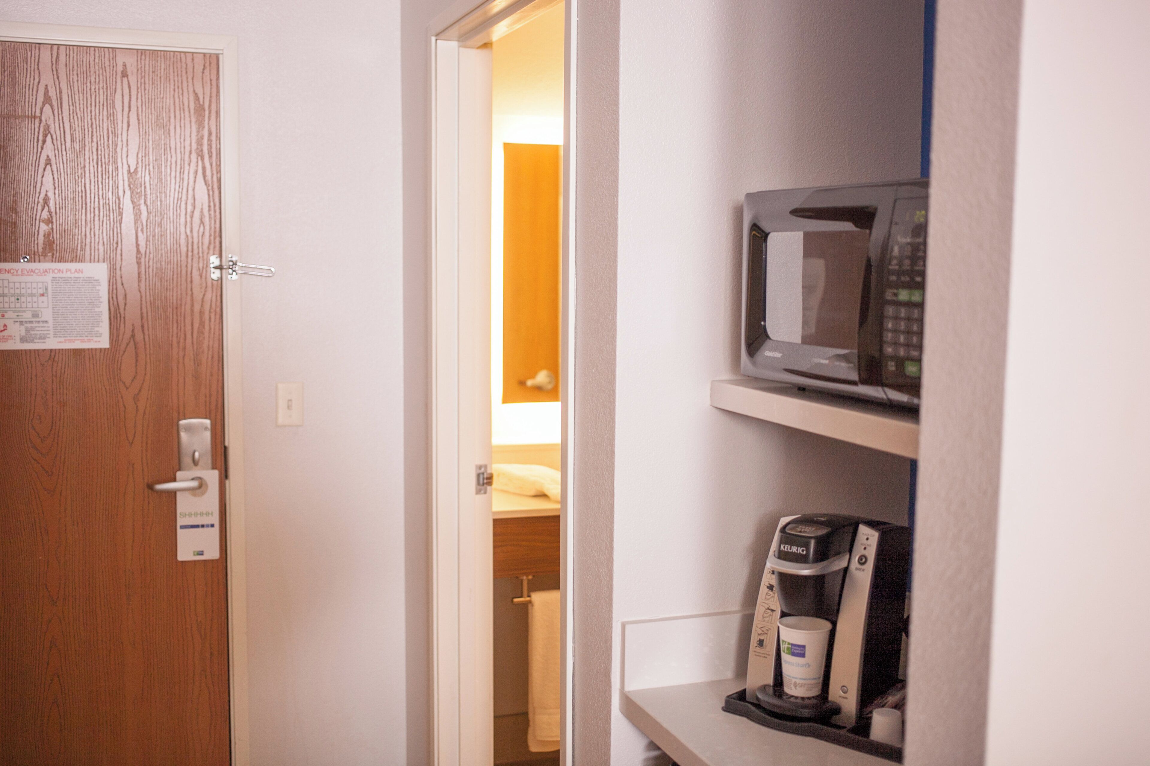 A hotel room with a wooden door, a visible energy evacuation plan, a microwave, and a coffee maker.