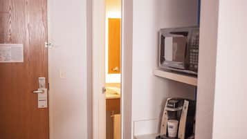 A hotel room with a wooden door, a visible energy evacuation plan, a microwave, and a coffee maker.