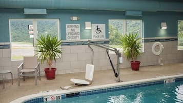An indoor swimming pool with a lifeguard warning sign, a pool lift, and chairs.