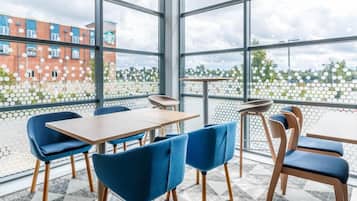 A modern indoor seating area with large windows, a patterned floor, and a view of a brick building.