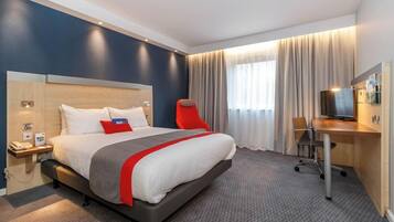 A hotel room with a bed, a desk, a chair, a television, and a window with curtains.