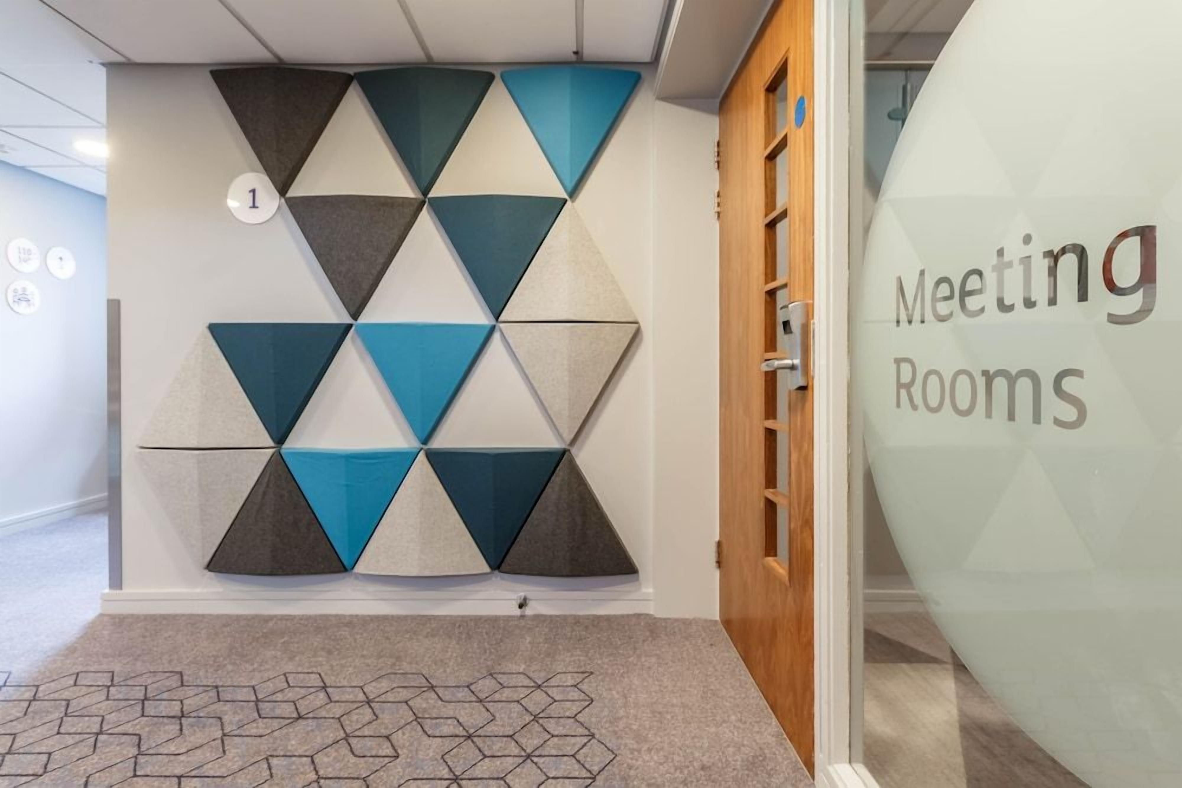 A hallway with a geometric wall design, a numbered sign, and a glass door labeled 'Meeting Rooms'.