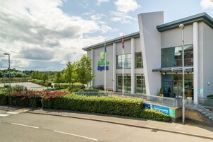 Un edificio de Holiday Inn Express con un diseño moderno, amplias ventanas y un área de entrada ajardinada.