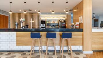 A modern bar area with a black countertop, three blue bar stools, and a variety of bottles and glasses.