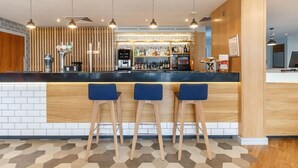 A modern bar area with a black countertop, three blue bar stools, and a variety of bottles and glasses. - Holiday Inn Express Birmingham - Walsall (Walsall)