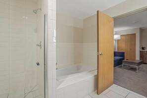 A modern bathroom with a glass shower enclosure, a bathtub, and a wooden door leading to a living area with a sofa and a coffee table. - Holiday Inn Express & Suites Torrington (Torrington)