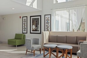Una sala de estar moderna con un sillón verde, sillones grises, un sofá marrón y dos mesas redondas.