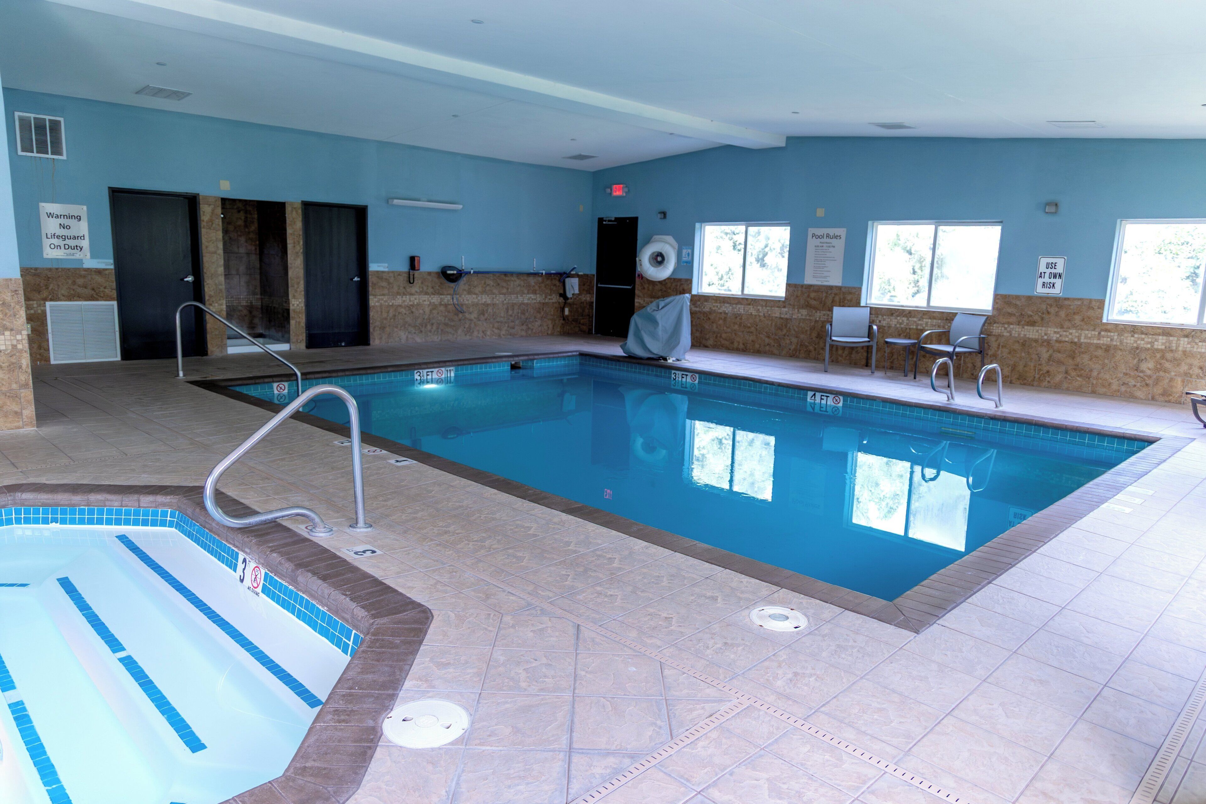 A swimming pool with a diving board, lifeguard on duty sign, and pool rules sign.