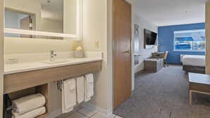 Une chambre d’hôtel moderne dotée d’un grand miroir, d’une coiffeuse en bois, d’un téléviseur à écran plat, d’un lit et d’un bureau.