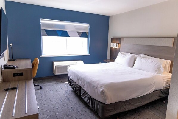 Habitación de hotel con cama, escritorio, silla, teléfono y ventana con persianas.