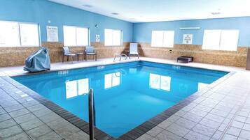 An indoor swimming pool with clear pool rules and no diving allowed signs, surrounded by tiled walls and a tiled floor.