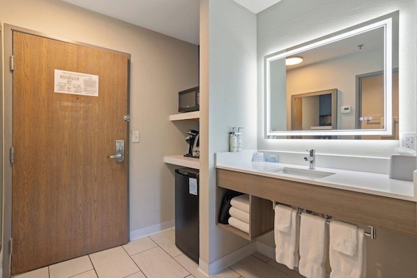 A bathroom with a wooden door, a microwave, a sink with a mirror, and towels. - Holiday Inn Express & Suites Torrington (Torrington)