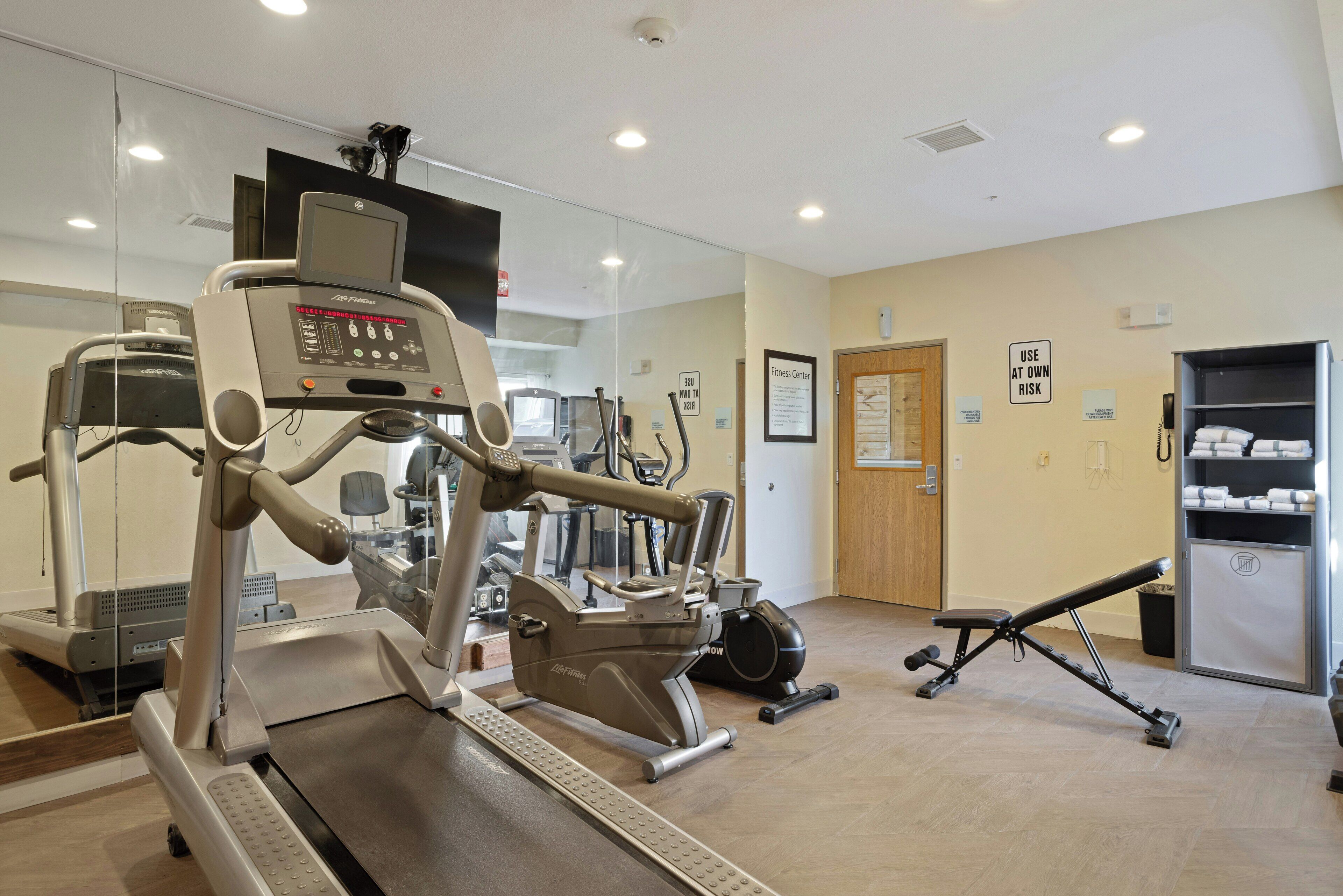 A gym with cardio machines, a bench press, and a wall-mounted sign indicating the use of the equipment at one's own risk.