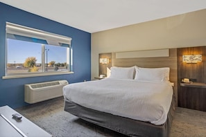 A modern hotel room with a large bed, a window with a view, a bedside table, and a wall-mounted lamp. - Holiday Inn Express & Suites Torrington (Torrington)