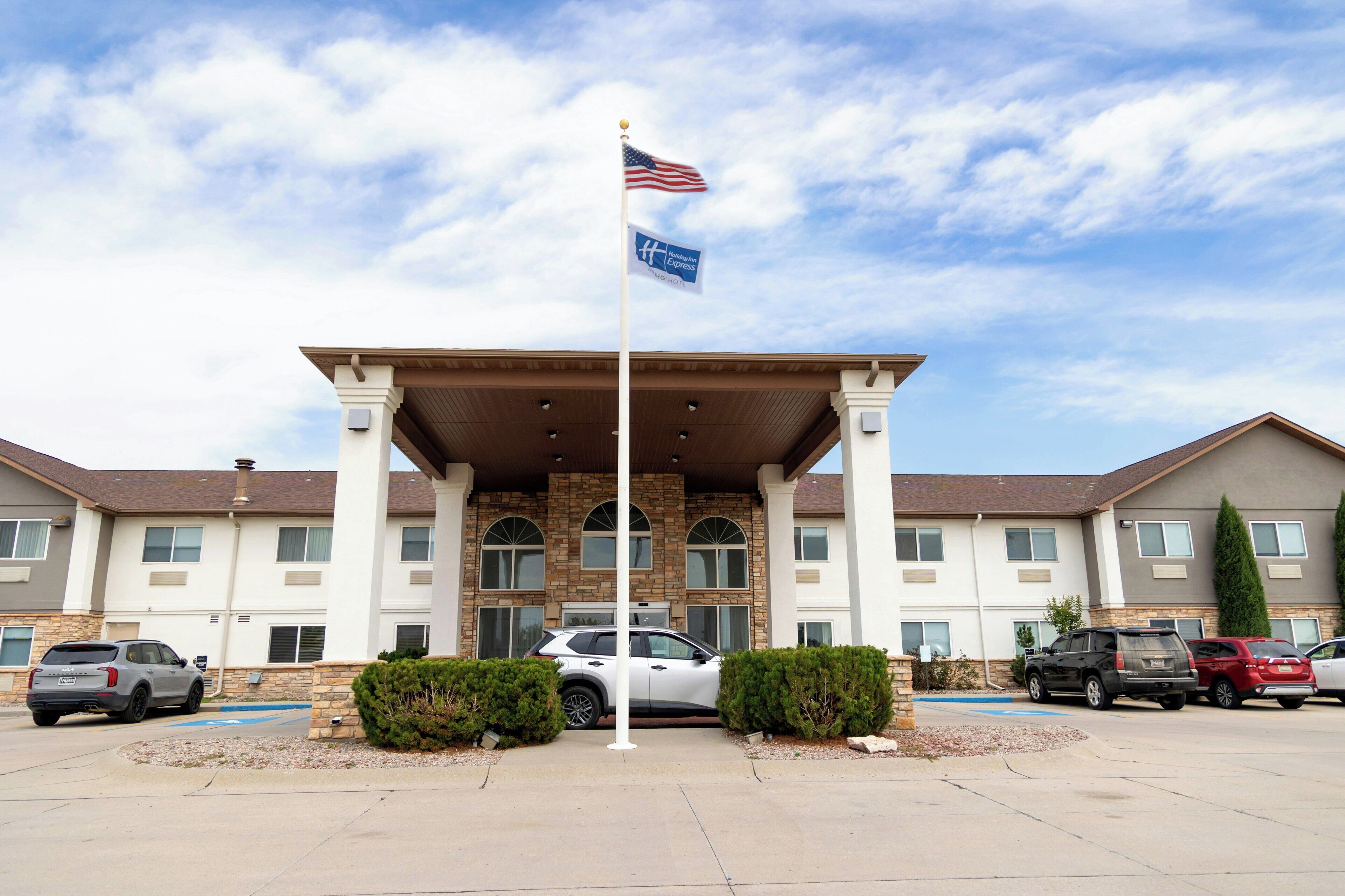 A hotel entrance with a flag, a covered parking area, and several parked cars.