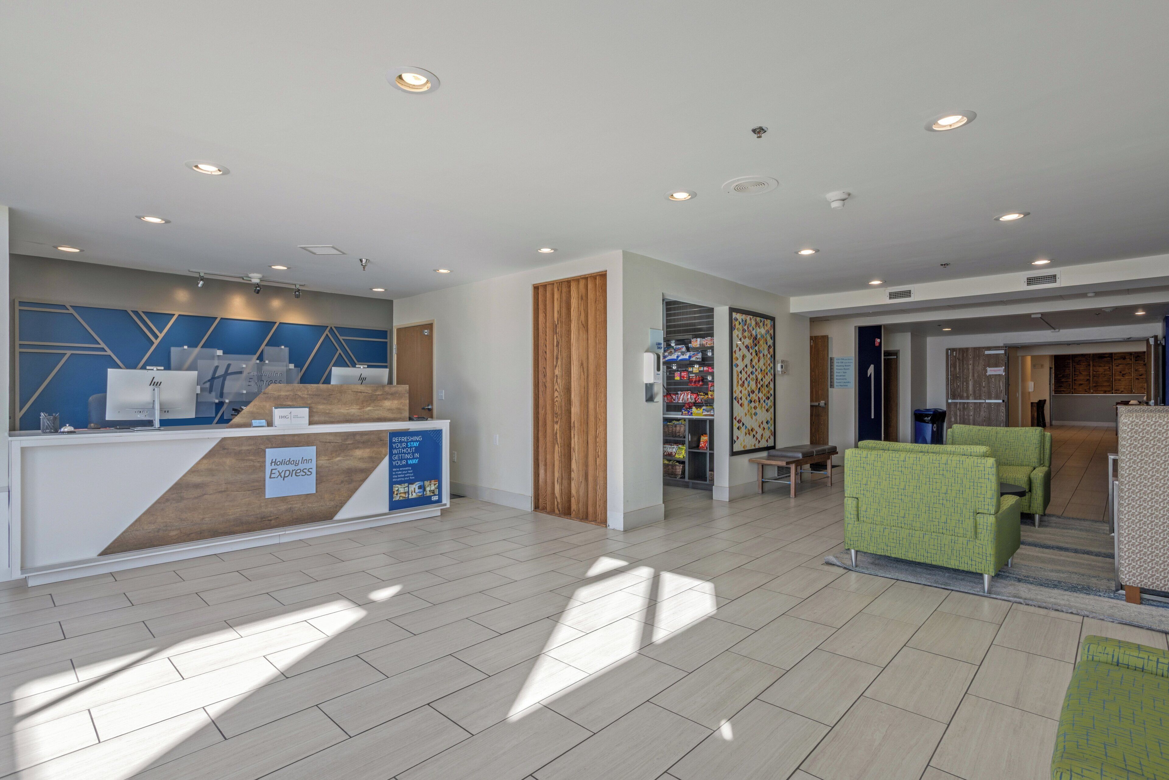 A hotel reception area with a modern design, including a reception desk, a seating area with green sofas, and a visible storage room in the background.