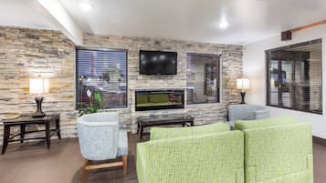 A living room with a stone wall, a flat-screen TV, a fireplace, and green upholstered sofas.