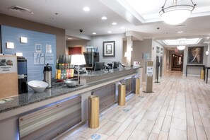 A hotel reception area with a counter, coffee station, and a hallway leading to the exit.