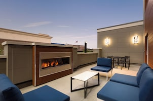 An outdoor patio area with a built-in fireplace, blue seating, and a dining table.