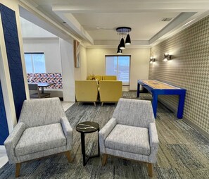 A room with two armchairs, a small table, a pool table, and a dining area with yellow chairs. - Holiday Inn Express and Suites Tuscaloosa University an IHG Hotel (Tuscaloosa)